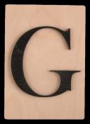 Holzplatte mit dem Buchstaben G in schwarzer Schrift. Der Hintergrund ist hell.