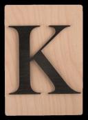 Holzplatte mit schwarzem Buchstaben K. Der Hintergrund ist hell und glatt.