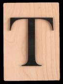 Holzplatte mit schwarzem Buchstaben 'T' darauf. Der Buchstabe ist groß und klar sichtbar.