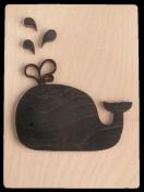 Schwarze Holzfigur eines Wals mit Wasserfontänen. Auf hellem Holzuntergrund.
