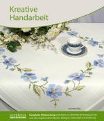 Tischdecke mit blauen Blumenstickereien. Eine Kaffeetasse auf einem Unterteller ist darauf platziert.