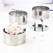 Drei runde Metallformen für Desserts. Eine Form gefüllt mit Schokoladenkuchen und Sahne, dekoriert mit rosa Zuckerperlen. Die anderen zwei Formen sind leer.