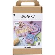 Starter-Kit für Häkelarbeiten. Zwei gehäkelte Taschen in Pastellfarben. Zubehör wie Wolle und Häkelnadel sichtbar. Anleitung zum Erlernen der Grundtechniken.