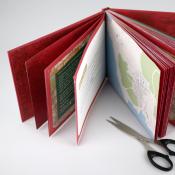 Offenes Buch mit roten Seiten und einer Karte auf der rechten Seite. Ein Paar Schere liegt daneben.