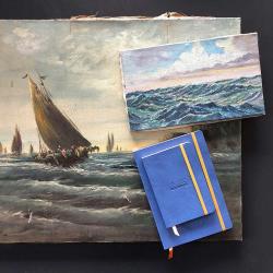 Zwei Gemälde mit maritimen Motiven. Ein Notizbuch in Blau liegt daneben.