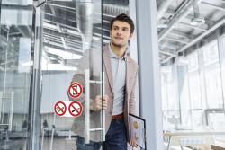 Mann in einem hellen Blazer, der eine Glastür öffnet. Im Hintergrund ein modernes Büro mit großen Fenstern.