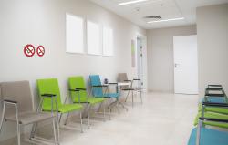 Wartezimmer mit mehreren Stühlen in Grün und Beige. An der Wand sind zwei Verbotsschilder.