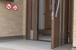 Eingangstür mit Holzoptik. Zwei Rauchverbotsschilder sind an der Wand angebracht.