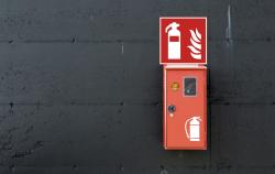 Rote Feuerlöschbox an einer schwarzen Wand. Oben ein Symbol für Feuerlöscher und Feuer.