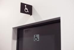 Tür mit einem Symbol für barrierefreies WC. Über der Tür ein weiteres Symbol für Rollstuhlfahrer.