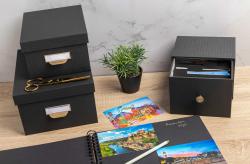 schwarze Aufbewahrungsbox mit goldener Knopföffnung. Quadratische Form, matte Oberfläche.