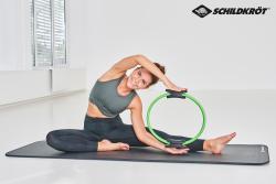 Ein grüner Pilates-Ring mit schwarzen Griffen. Der Ring hat eine runde Form.