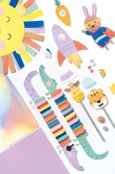 Bastelbox mit bunten Papierfiguren. Enthält Pinguine, Fische, ein Tier mit Pullover und Bastelmaterialien. Farbenfroh und kinderfreundlich.