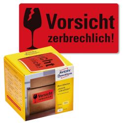 Rote Warnetiketten mit dem Text 'Vorsicht zerbrechlich!'. Verpackung zeigt eine gelbe Box mit Etiketten für den Paketversand.