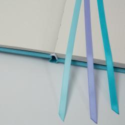 Offenes Notizbuch mit gepunktetem Papier. Drei farbige Bänder in Blau und Lila sind sichtbar.