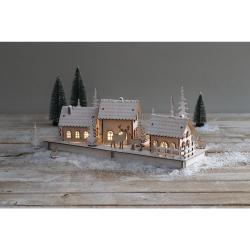 Holzmodell eines winterlichen Dorfes mit drei Häusern und Tannenbäumen. Zwei Rehe stehen auf der Basis.