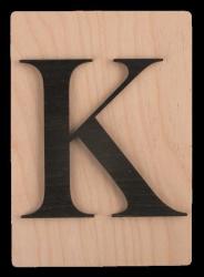 Holzplatte mit schwarzem Buchstaben K. Der Hintergrund ist hell und glatt.