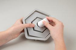 Siliconform für einen hexagonalen Kerzenständer. Farbe: Weiß. Enthält eine schwarze Holzfigur in Form eines Hauses. Kerze in der Mitte. Herzmotiv auf der Basis.
