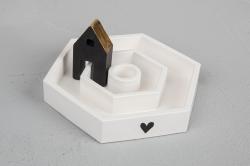 Siliconform für einen hexagonalen Kerzenständer. Farbe: Weiß. Enthält eine schwarze Holzfigur in Form eines Hauses. Kerze in der Mitte. Herzmotiv auf der Basis.