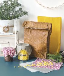 Braune Papiertüte mit Muster, gelbe Papiertüte im Hintergrund. Zwei Gläser mit Stoffdeckeln, eines mit Bienenwachs.