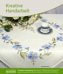 Tischdecke mit blauen Blumenstickereien. Eine Kaffeetasse auf einem Unterteller ist darauf platziert.