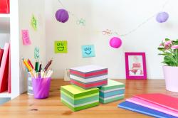 Bürotisch mit bunten Notizblöcken und Stiften. Dekorative Laternen und ein Pflanzengefäß sind sichtbar.