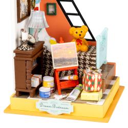 Miniaturzimmer mit Bett, Leiter und Tisch. Bunte Wände, Bilderrahmen, Lampe. Spielzeugbär auf dem Bett. Malerei auf Staffelei. Bücherregal und Geschenke.