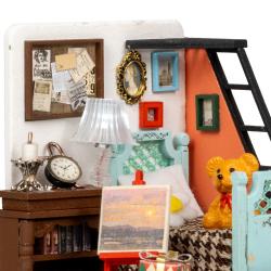 Miniaturzimmer mit Bett, Leiter und Tisch. Bunte Wände, Bilderrahmen, Lampe. Spielzeugbär auf dem Bett. Malerei auf Staffelei. Bücherregal und Geschenke.