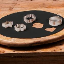 Verpackung für schwarzen, vorgerollten Zuckerteig. Abgebildete Hände formen Teig mit Ausstechformen. Holzplatte im Hintergrund.