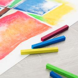 Packung mit 24 harten Pastellkreiden. Bunte Kreiden liegen auf einem farbigen Hintergrund.