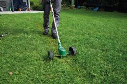 Grüner elektrischer Rasentrimmer mit zwei großen Rädern. Langer Griff und ergonomischer Handgriff.