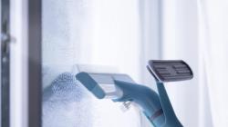 Fenstersauger mit blauer Halterung und transparentem Behälter. Hat einen Sprühmechanismus.