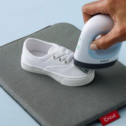 Weiße Sneaker auf einem grauen Untergrund. Eine Hand hält ein Gerät, das auf die Schuhspitze gerichtet ist.