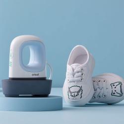 Ein kleiner, weißer Heizpresse von Cricut. Neben der Presse steht ein weißer Schuh mit einem Tiermotiv auf der Vorderseite.