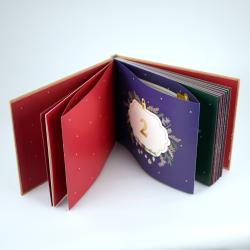 Offenes Buch mit bunten Seiten, die eine festliche Gestaltung zeigen. Die Seiten sind rot, grün und blau mit goldenen Akzenten.