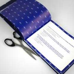 Offenes Heft mit blauer Coverseite, darin sind Textaufgaben in Deutsch und Geschichte. Ein Paar schwarze Schere liegt auf dem Heft.