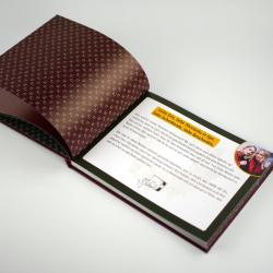 Offenes Buch mit dunklem Einband und Muster auf den Seiten. Auf der rechten Seite ein Textfeld mit Begrüßung und einem kleinen Foto in der Ecke.