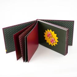 Offenes Fotobuch mit schwarzen, roten und weißen Seiten. Auf einer Seite sind zwei kleine Figuren in einem Sternhintergrund angebracht.