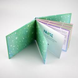 Aufklappbares Buch mit buntem Winterdesign. Innen sind Seiten mit Text und farbigen Hintergründen sichtbar.