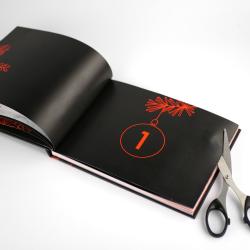 Offenes Buch mit schwarzem Hintergrund und roten Designelementen. Seite zeigt eine große rote Zahl eins und eine stilisierte Weihnachtsbaum- oder Tannenzweigdarstellung.