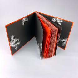 Offenes Buch mit schwarzem Hintergrund und weißen Tannenzweigen. Die Seiten sind rot und schwarz gestaltet.