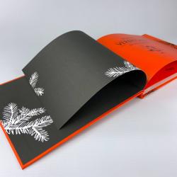 Offenes Buch mit schwarzem und orangefarbenem Cover. Weiße Pflanzenmuster auf den Seiten, die Farben sind kräftig.