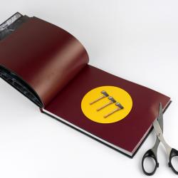 Offenes Buch mit dunkelroten Seiten. Auf der Seite sind drei kleine Äxte auf einem gelben Kreis abgebildet.