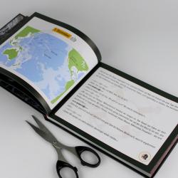 Offenes Buch mit Weltkarte auf der linken Seite und Text auf der rechten Seite. Ein Messer liegt darunter.