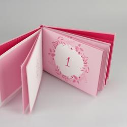 Kleines, aufklappbares pinkes Fotobuch mit Weihnachtsmotiven und der Zahl eins auf der ersten Seite.