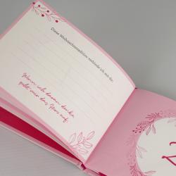Offenes pinkes Buch mit weihnachtlichem Design. Auf der linken Seite sind Linien für Notizen, darunter ein handgeschriebener Text.