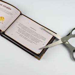 Offenes Buch mit Text und kleinen Illustrationen. Eine Schere liegt auf der rechten Seite des Buches.