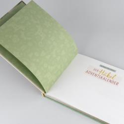 Offenes Buch mit gelbem und weißen Seiten. Auf einer Seite ist eine Tabelle mit Text, auf der anderen Seite ein Bild eines gehäkelten Schneemanns.