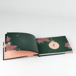 Offenes Fotobuch mit bunten, floralen Illustrationen auf dunkelgrünem Hintergrund. Eine Seite zeigt eine große Zahl eins in einem runden Rahmen.