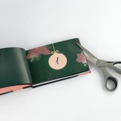 Offenes Buch mit grünen Seiten und einem weichen Einband. Eine Schere liegt daneben, vermutlich zum Schneiden.